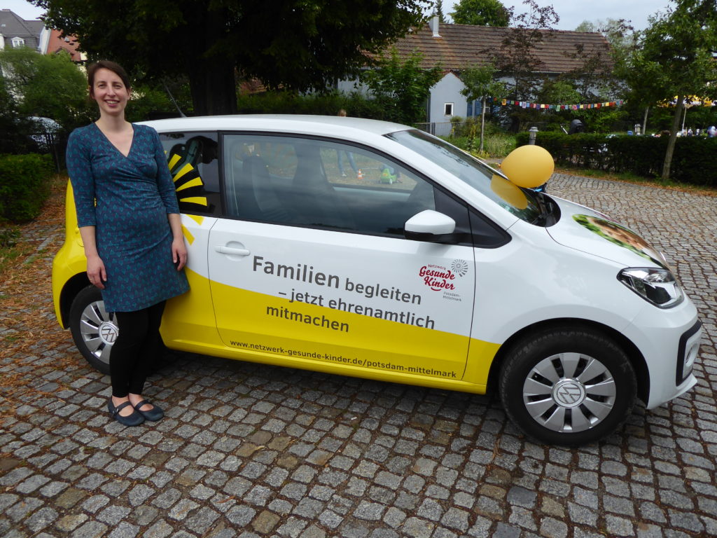 Netzwerkauto in weiß mit gelber Schnecke mit Aufschrift "Familien begleiten - Jetzt ehrenamtlich mitmachen" und Netzwerkkoordinatorin