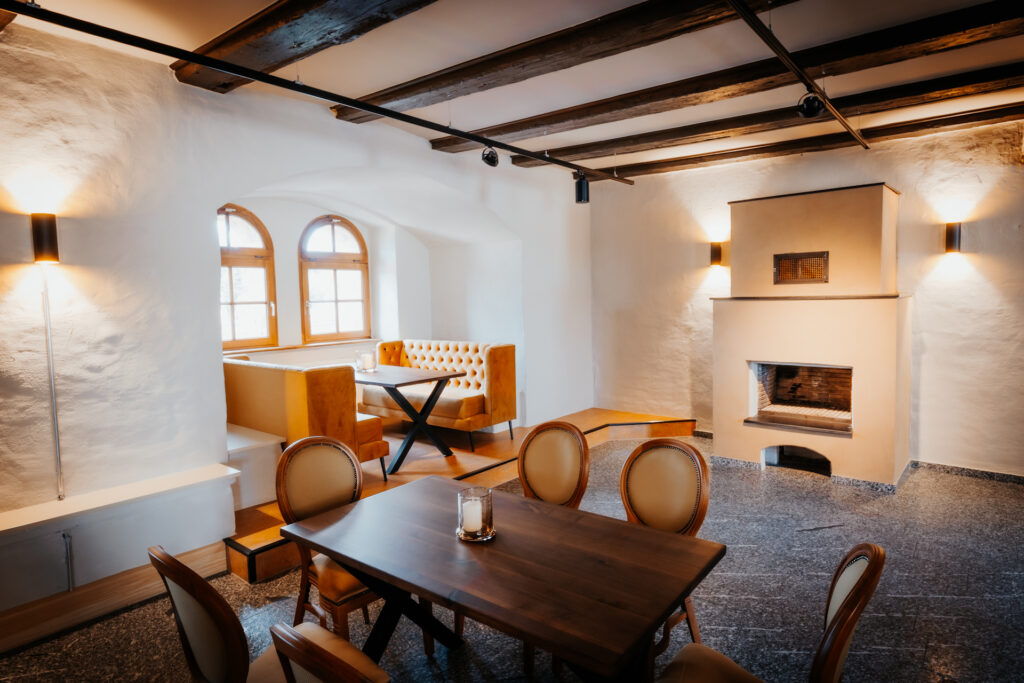 Restaurantraum mit Tisch für 6 Personen an 6 Stühlen, Tisch für 6 Personen auf 2 Couches, im Hintergrund Kamin